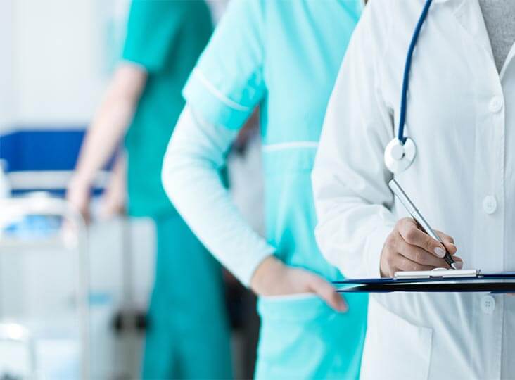 doctor in lab coat, with person in scrubs behind, torsos only
